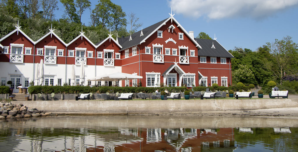 Dyvig Badehotel building in Als, Denmark. A red and white detailed historical building with a outdoor modern lounge area with lounge sofas from Cane-line.