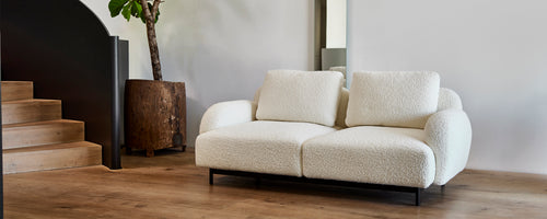 Canapé deux places moderne et confortable avec des coussins doux sur un cadre en métal élégant, accompagné d'un élégant pot de fleurs et d'une décoration minimaliste.