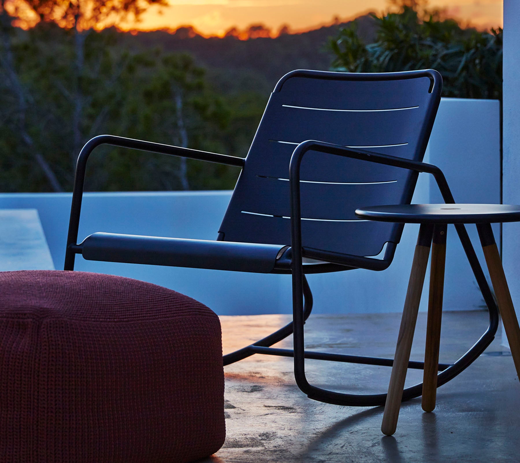 Chaise berçante élégante avec un cadre noir épuré et un coussin de siège gris, accompagnée d'une petite table d'appoint en bois et d'un pouf rond.