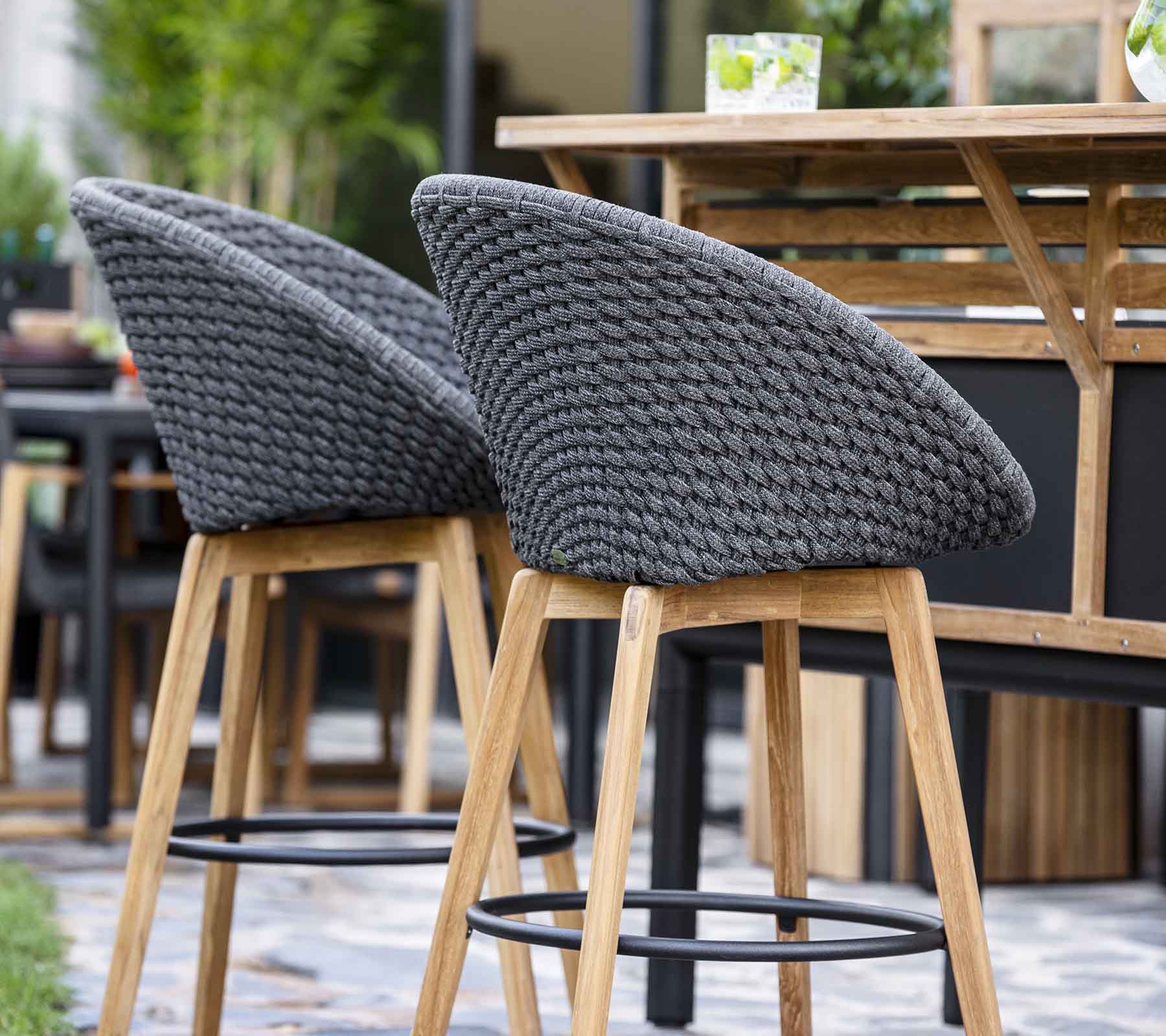 Tabourets de bar élégants avec des dossiers en tissu gris tissé et des pieds en bois, disposés près d'une table en bois dans un cadre contemporain.
