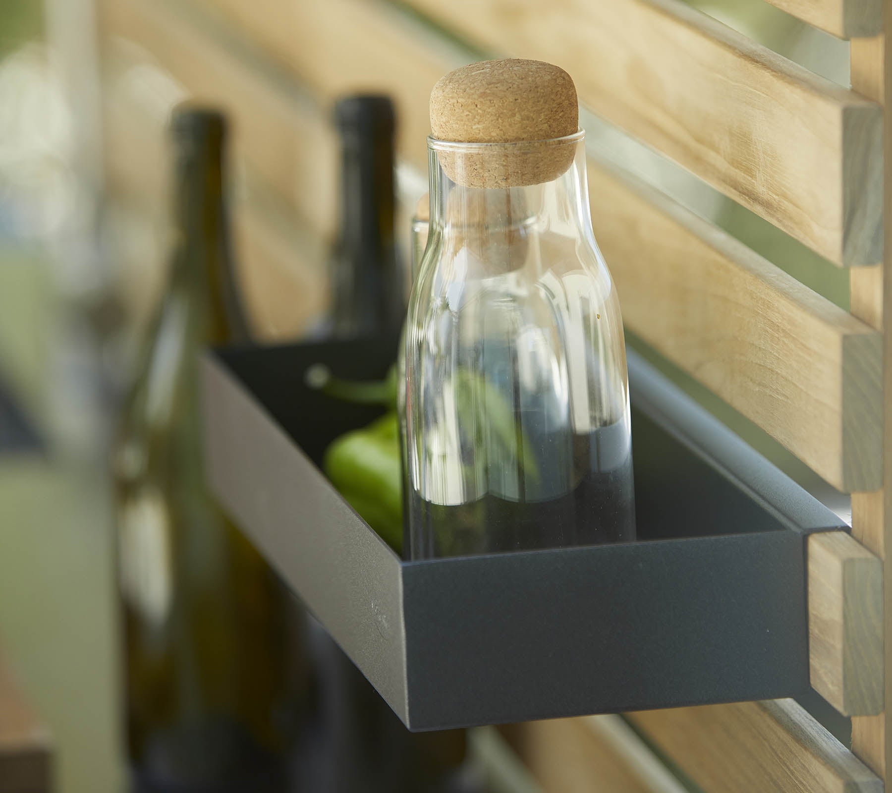 Une bouteille en verre avec un bouchon en liège est posée sur une étagère aux côtés de plusieurs bouteilles foncées, contre un fond en bois.