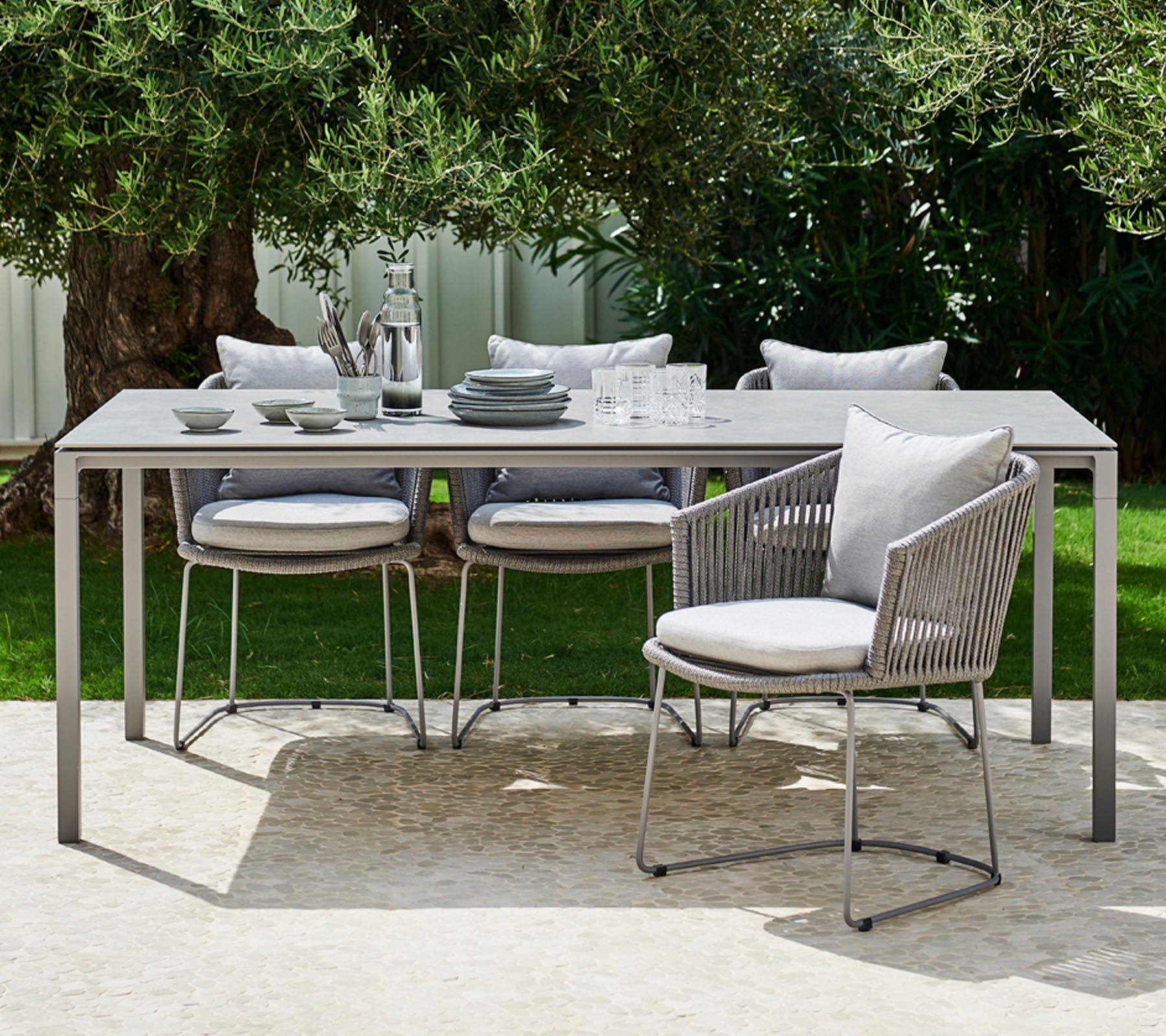 Un ensemble de salle à manger d'extérieur moderne comprenant une table épurée, des chaises rembourrées et de la vaisselle élégante disposée pour un repas stylé.
