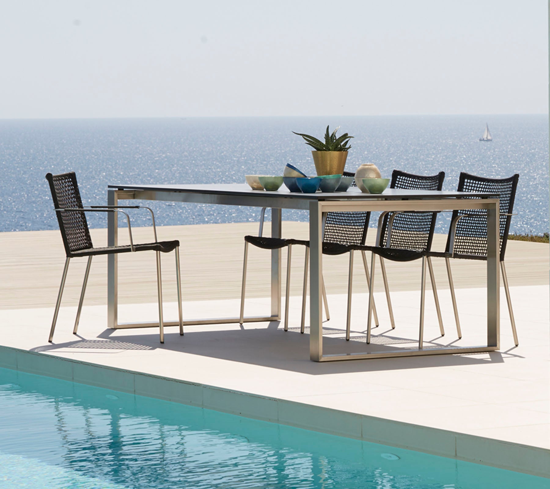 Une table à manger moderne entourée de chaises élégantes, ornée d'objets décoratifs, surplombant une vue mer tranquille.