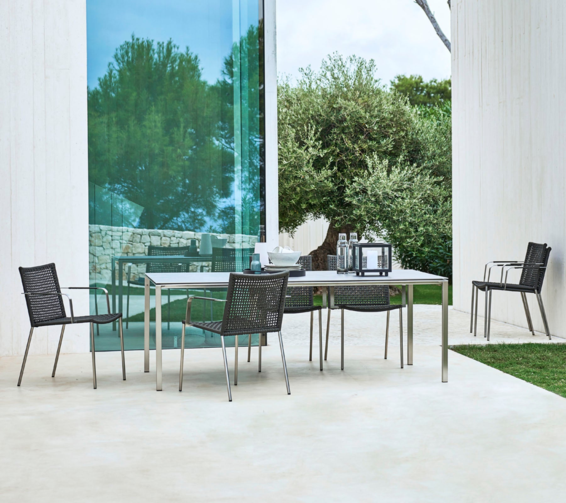 Un ensemble de repas d'extérieur moderne avec une table rectangulaire et quatre chaises élégantes au design épuré, entouré de verdure.