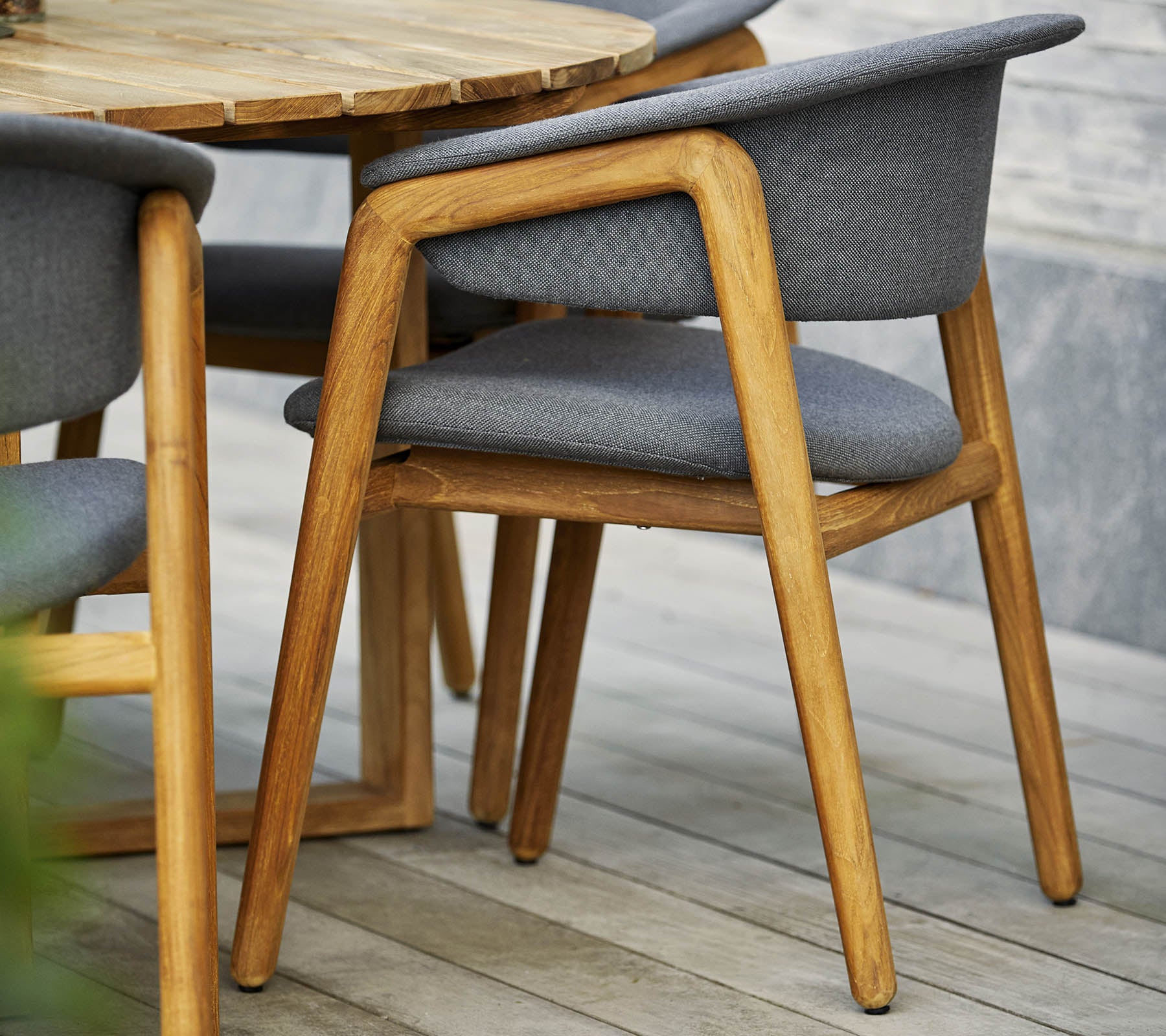 Chaise en bois élégante avec un siège et un dossier en tissu gris, associée à une table ronde au design contemporain.
