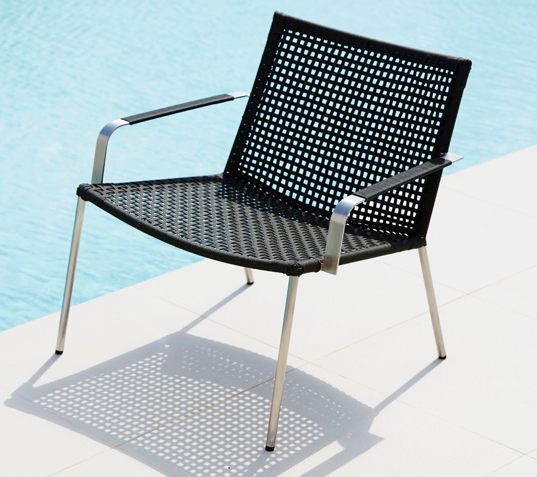 Chaise noire élégante avec un design perforé et des pieds en métal épurés, projetant une ombre sur une surface claire.