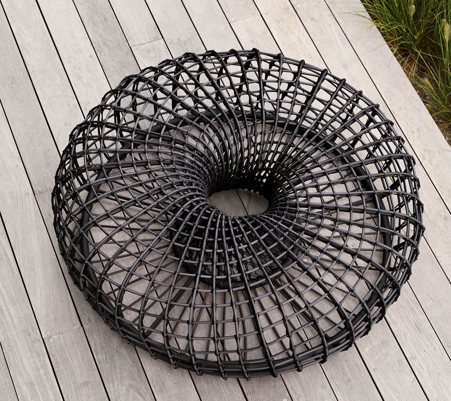 Panier en fil de fer noir moderne et circulaire avec un design en tissage ouvert unique, reposant sur une surface plane. Idéal pour le rangement ou des fins décoratives.