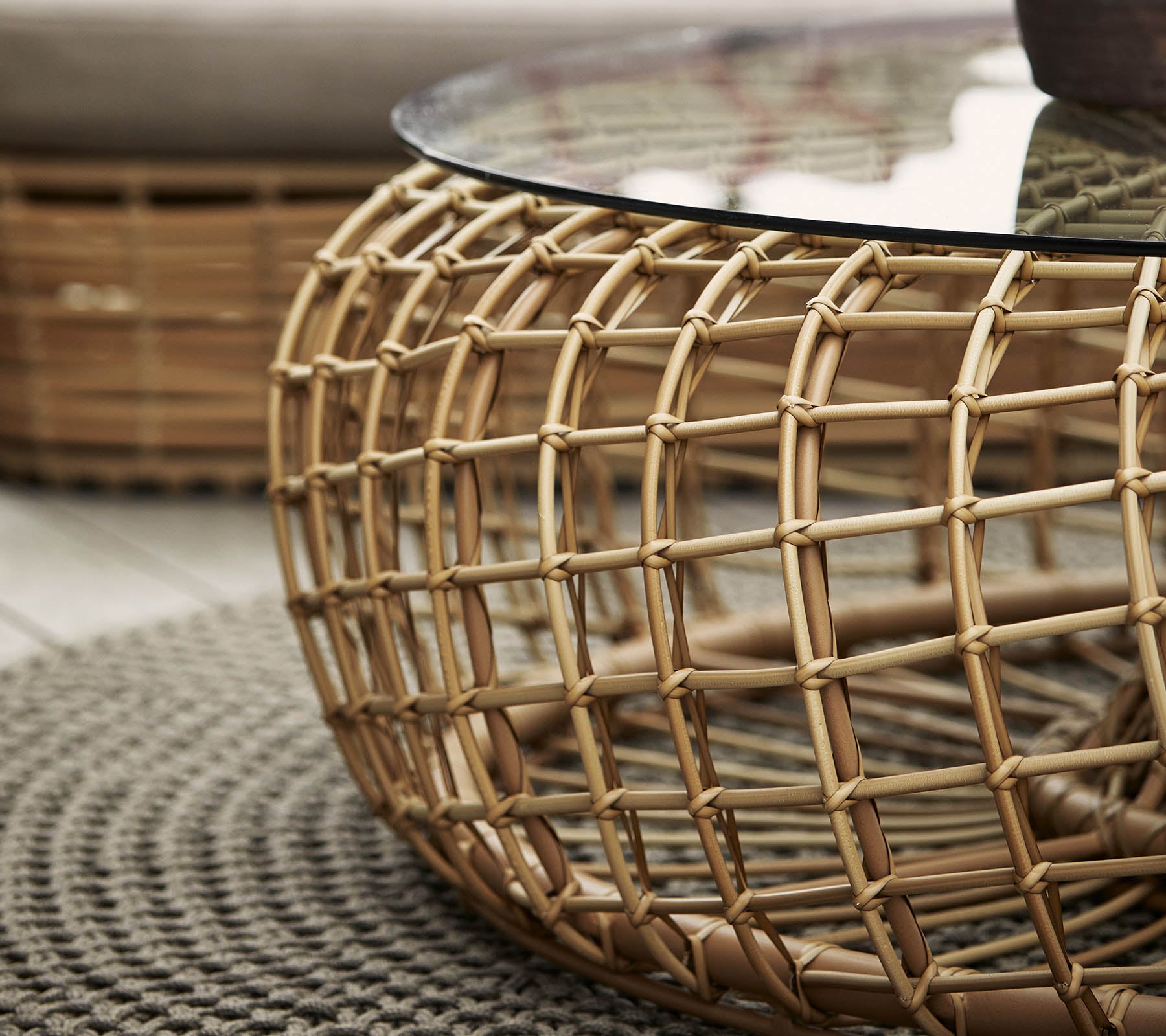 Table basse ronde avec une base en rotin tressé et un plateau en verre, complétée par un tapis circulaire texturé.