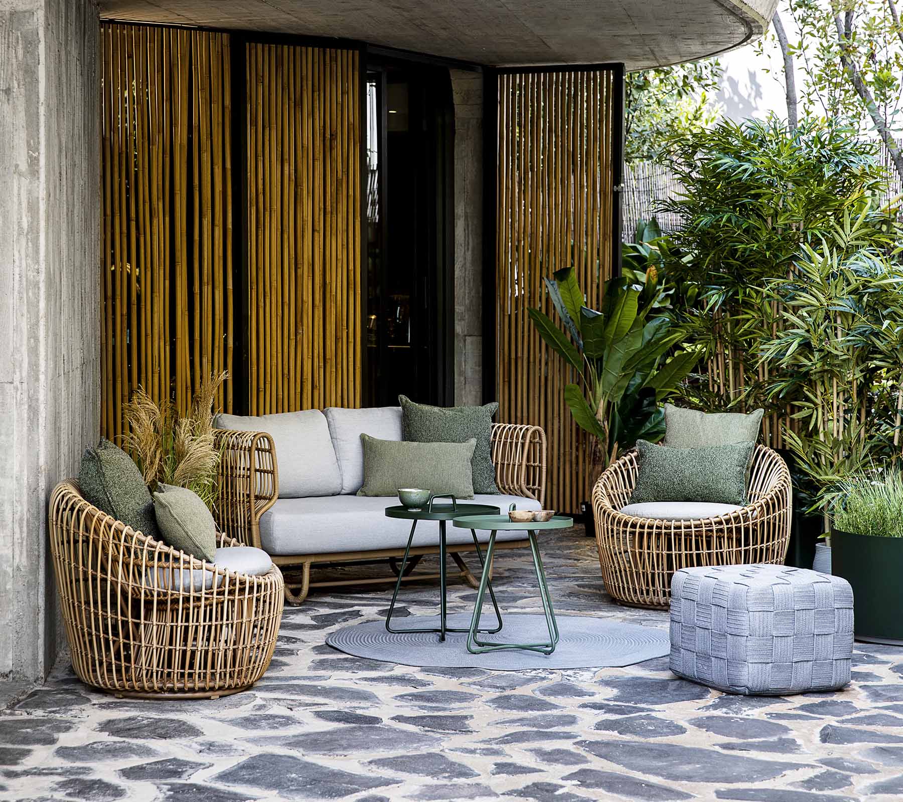 Espace de lounging élégant avec un canapé et des fauteuils ronds, agrémenté de coussins et une table basse, entouré de verdure.