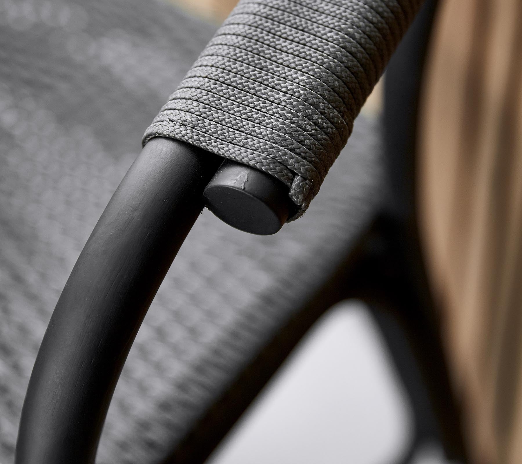 Gros plan d'un accoudoir de chaise élégant avec un cadre noir épuré et un revêtement gris texturé pour une prise confortable.