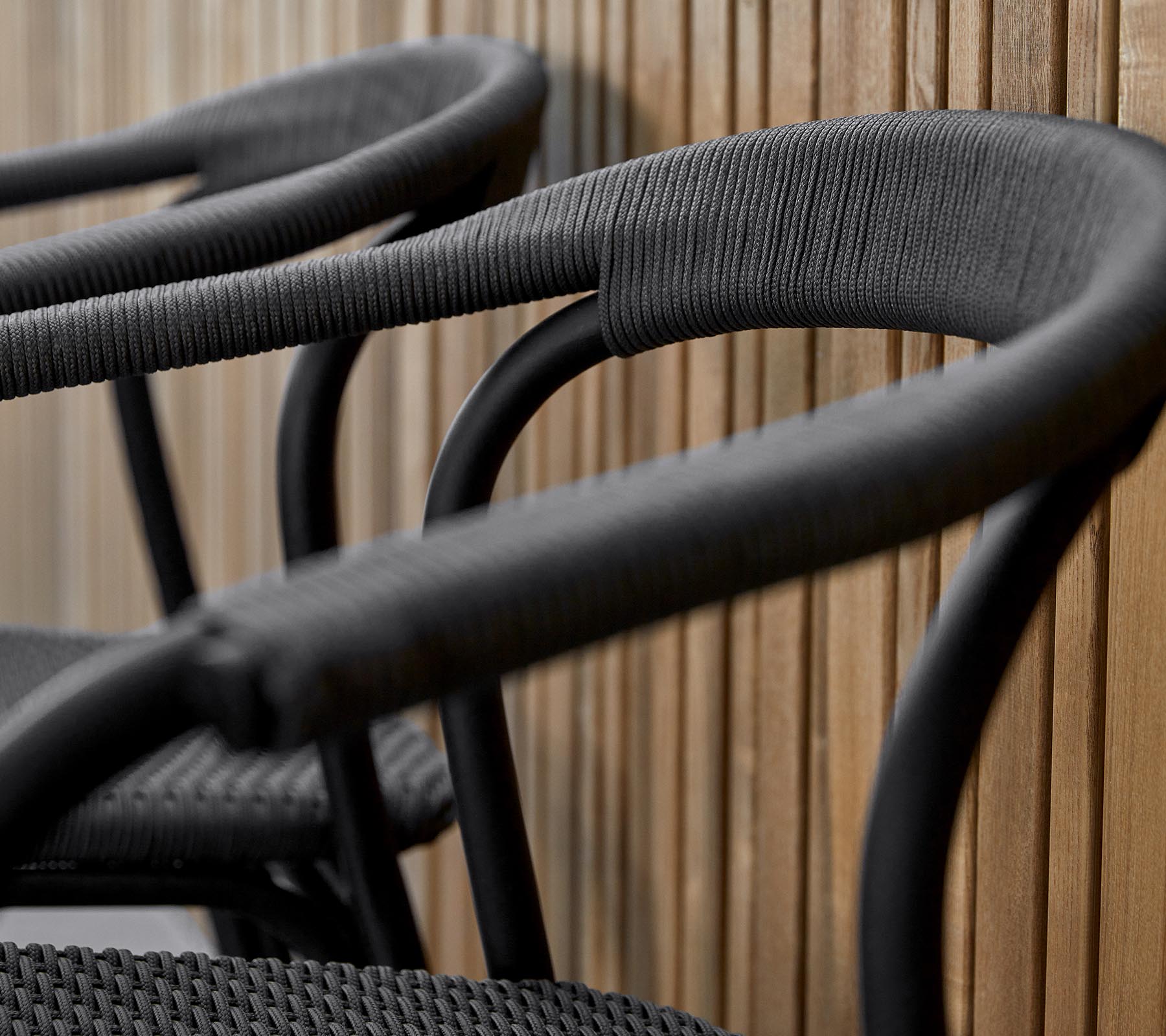 Trois chaises noires élégantes avec des accoudoirs incurvés, conçues avec une finition texturée, sur un fond chaud en bois.