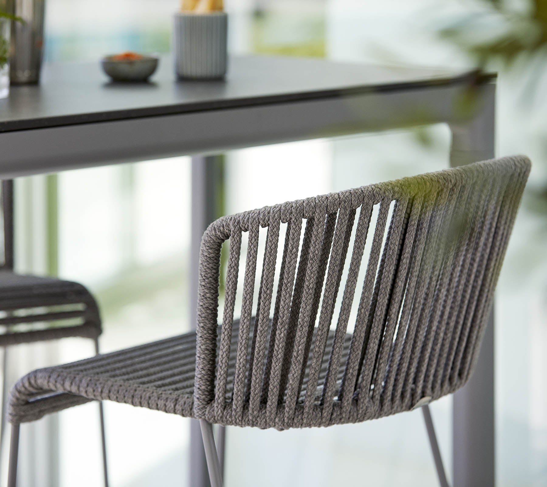 Chaise grise élégante au design épuré, avec des rayures verticales et une esthétique moderne, placée à côté d'une table minimaliste.