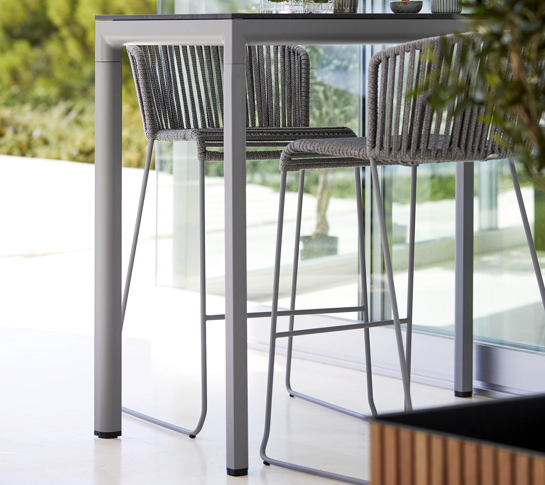 Une table élégante et moderne avec des chaises hautes assorties, présentant un design minimaliste et un cadre en métal élégant, complété par de la verdure naturelle.