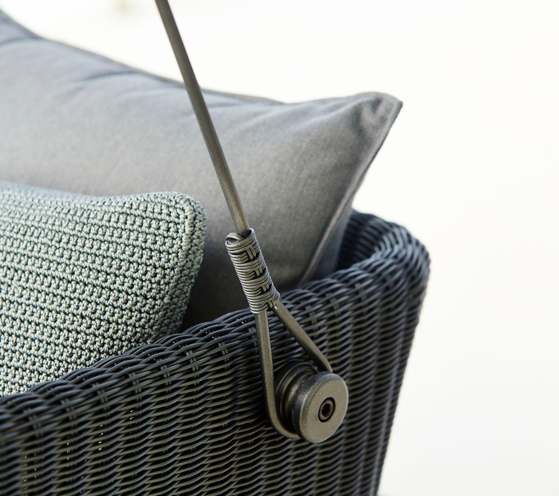 Gros plan sur un meuble d'assise tissé et élégant avec des coussins gris et un mécanisme de support épuré. Idéal pour une décoration moderne.