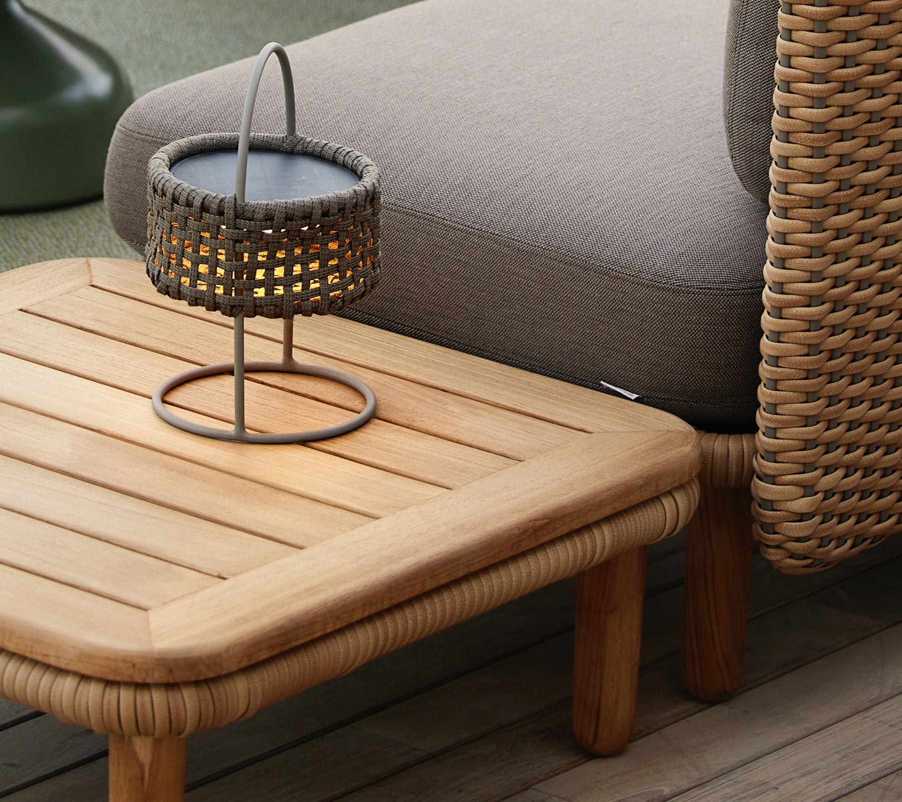Table basse en teck avec un dessus à lattes, accompagnée d'une lampe tissée, créant une atmosphère chaleureuse et accueillante.
