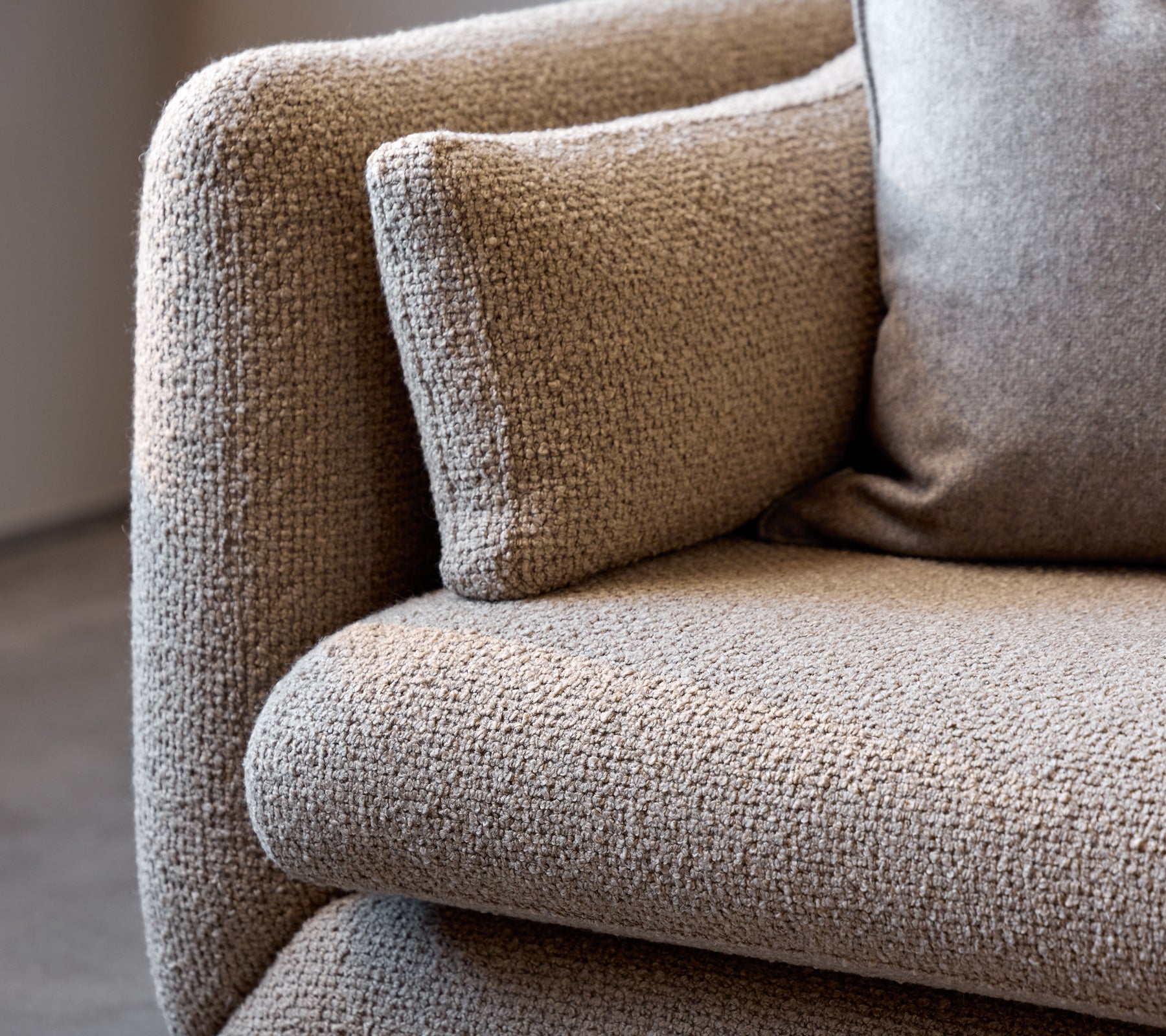 Gros plan d'un accoudoir de canapé Bloom taupe, mettant en valeur son tissu texturé et son coussin moelleux pour plus de confort.