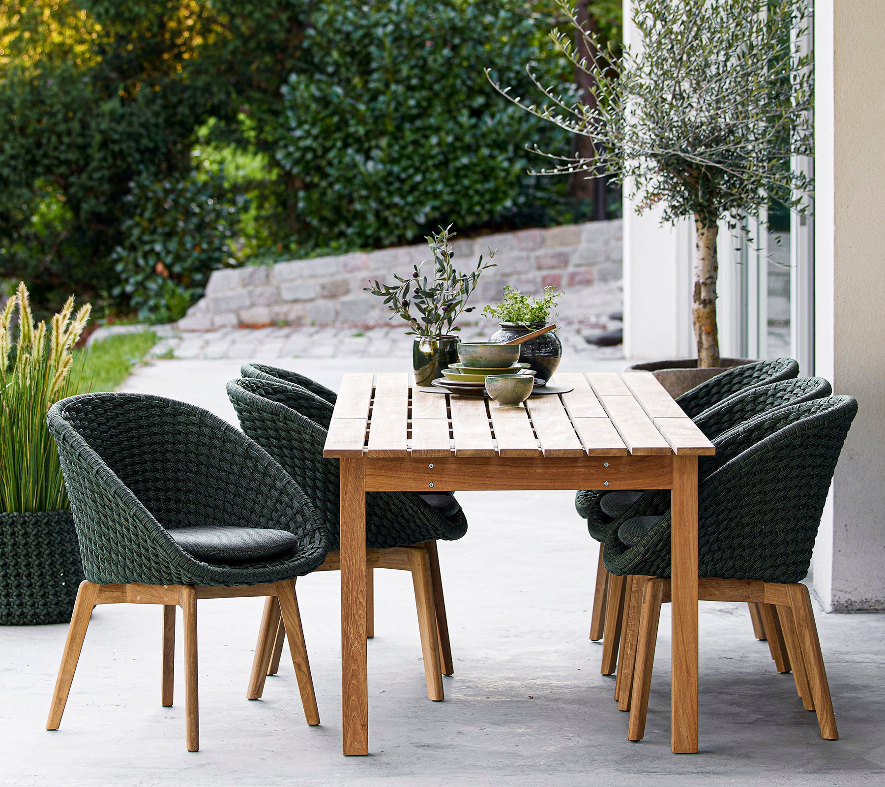 Une table en bois entourée de chaises vertes élégantes, avec des plantes décoratives et un arrière-plan serein. Idéal pour dîner ou se détendre.