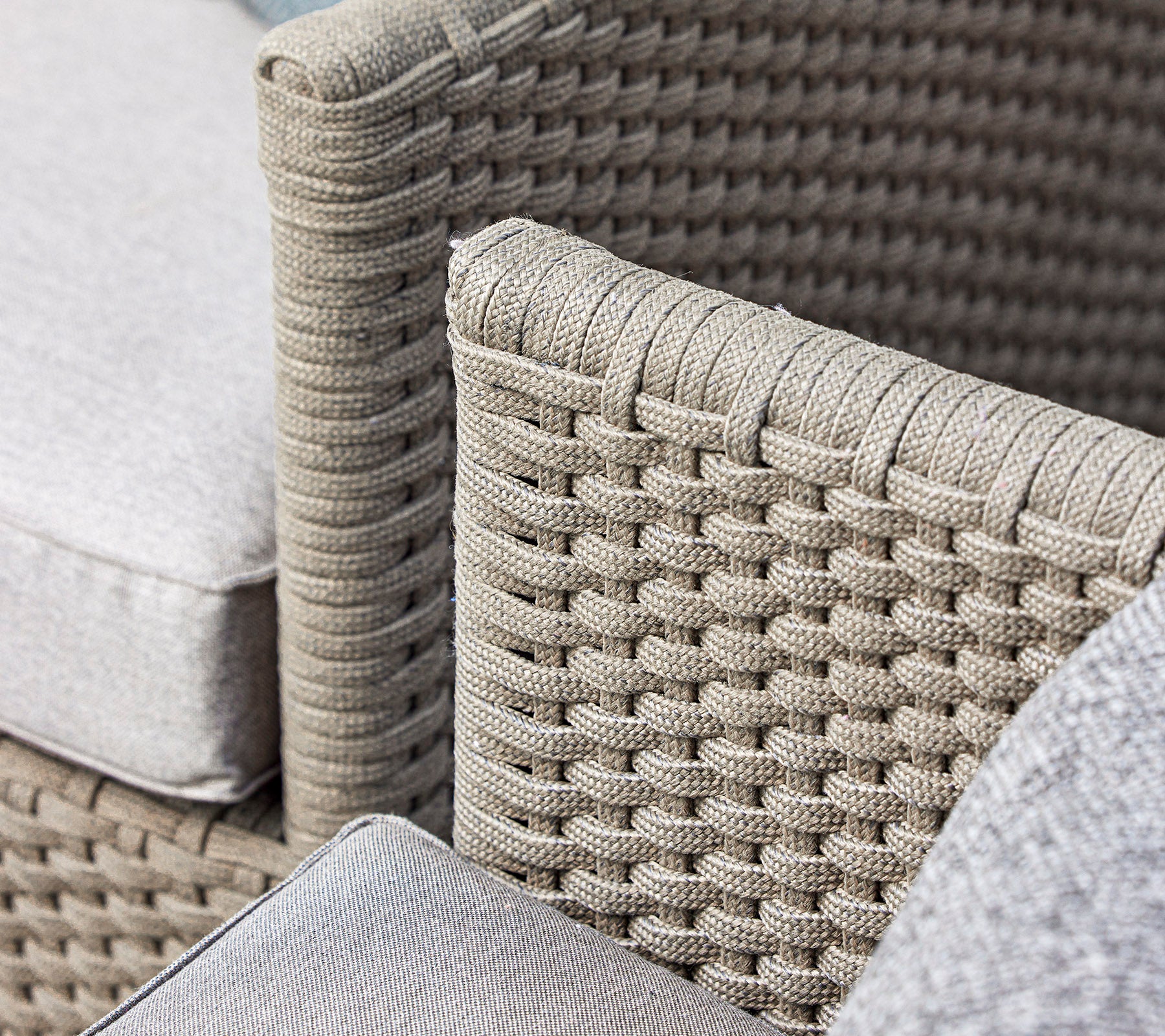 Gros plan d'un design de chaise en osier tissé avec des coussins doux dans une teinte neutre, mettant en valeur le savoir-faire et la texture.