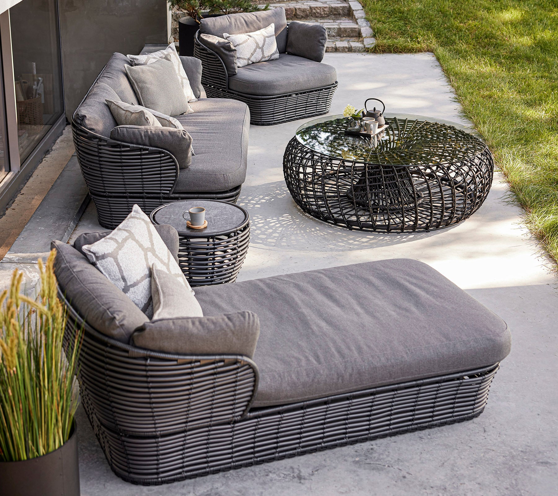 Aménagement de sièges extérieur élégant avec des meubles tressés, des coussins, une table basse en verre et des plantes décoratives. Idéal pour se détendre.