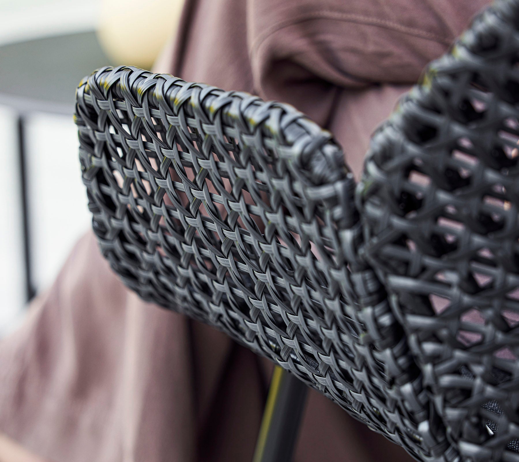 Dossier de chaise tissé noir avec un design texturé, complété par un tissu drapé en arrière-plan.