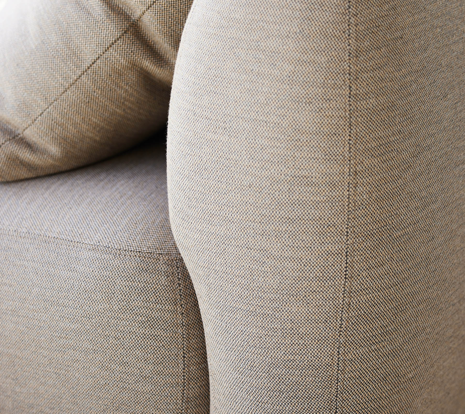 Gros plan d'un revêtement beige texturé, mettant en avant l'accoudoir incurvé et les coussins moelleux d'un meuble.