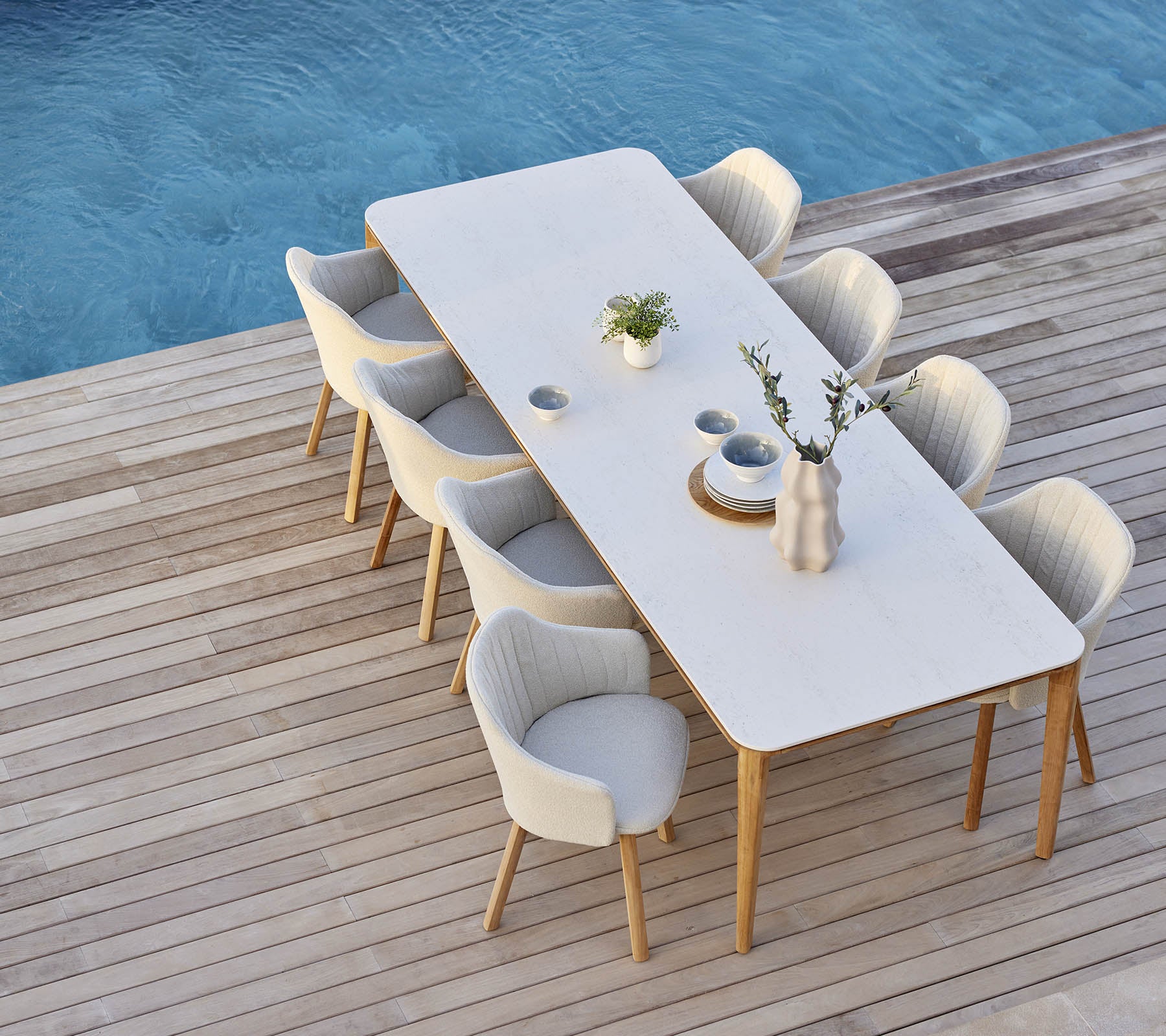 Configuration de salle à manger élégante avec une longue table entourée de chaises confortables, ornée d'un vase et d'accents de plantes.