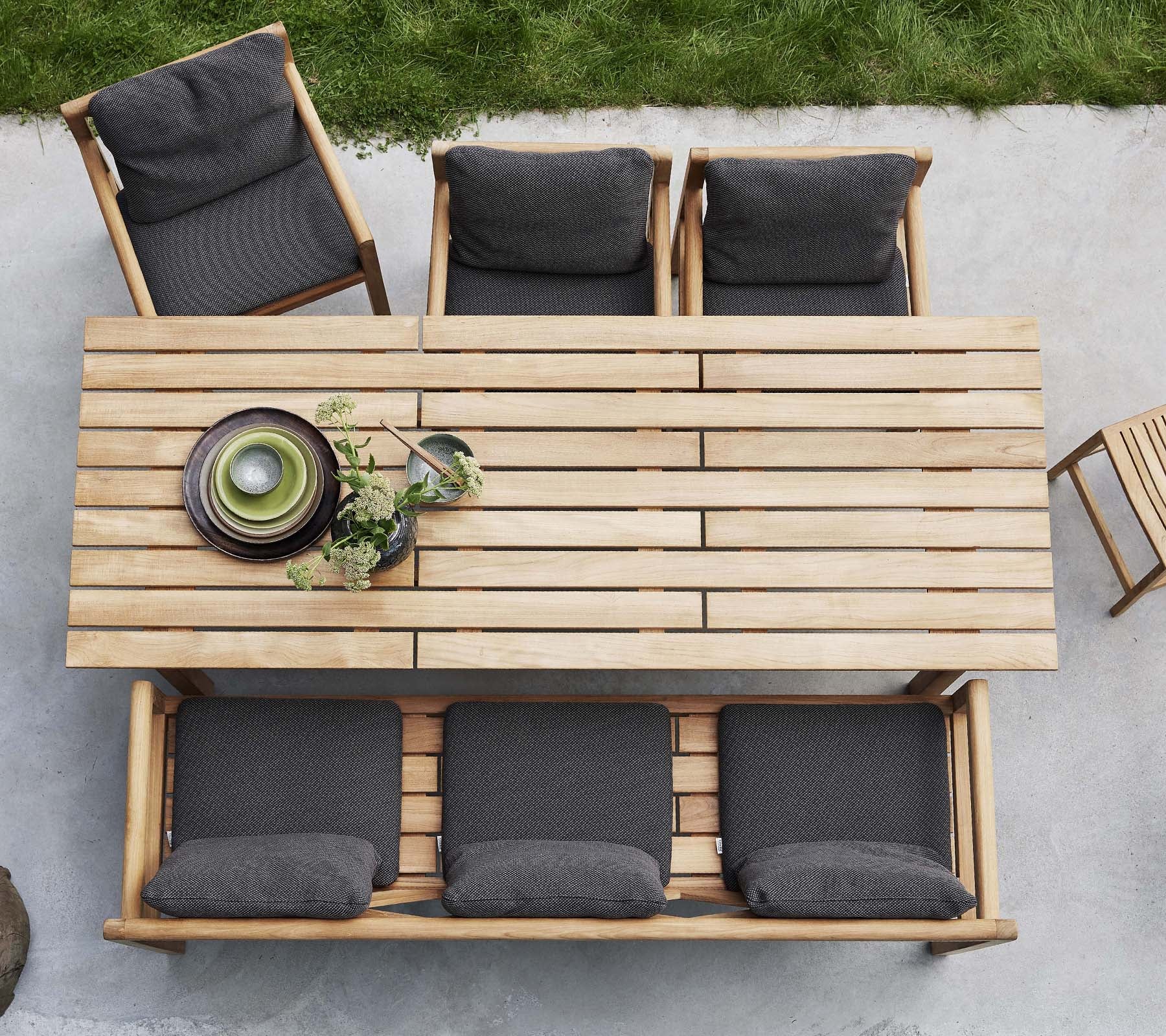 Une table en bois accompagnée de quatre chaises, chacune avec des coussins foncés, présentant des assiettes décoratives et de la verdure sur la table.