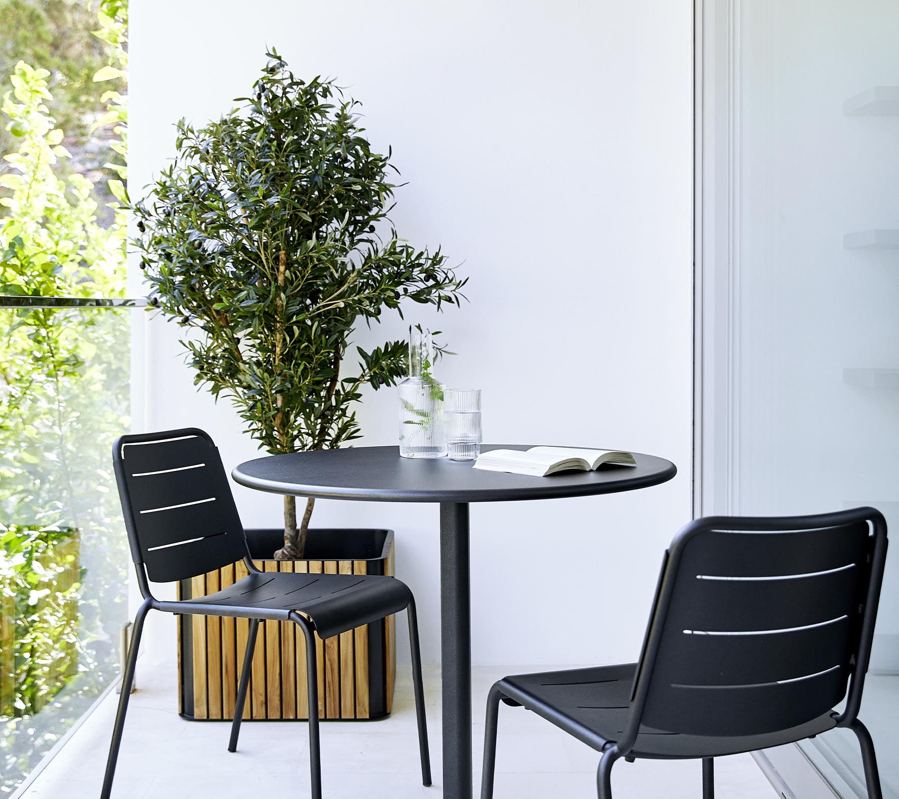 Un aménagement de salle à manger moderne comprenant une table ronde, deux chaises noires et une plante en pot, créant une atmosphère élégante et accueillante.