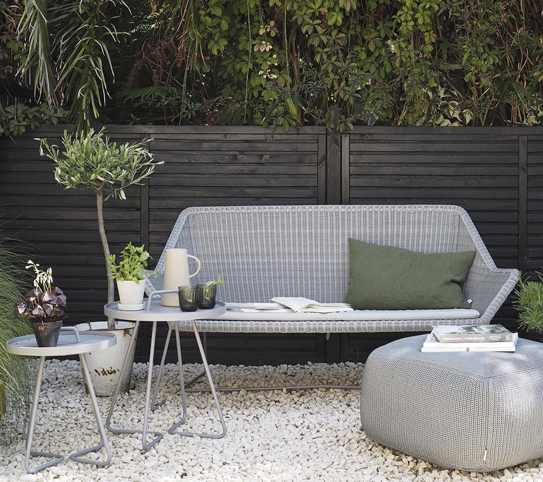 Agencement de meubles d'extérieur minimaliste avec un canapé élégant, des tables d'appoint et des plantes décoratives sur un sol en gravier.