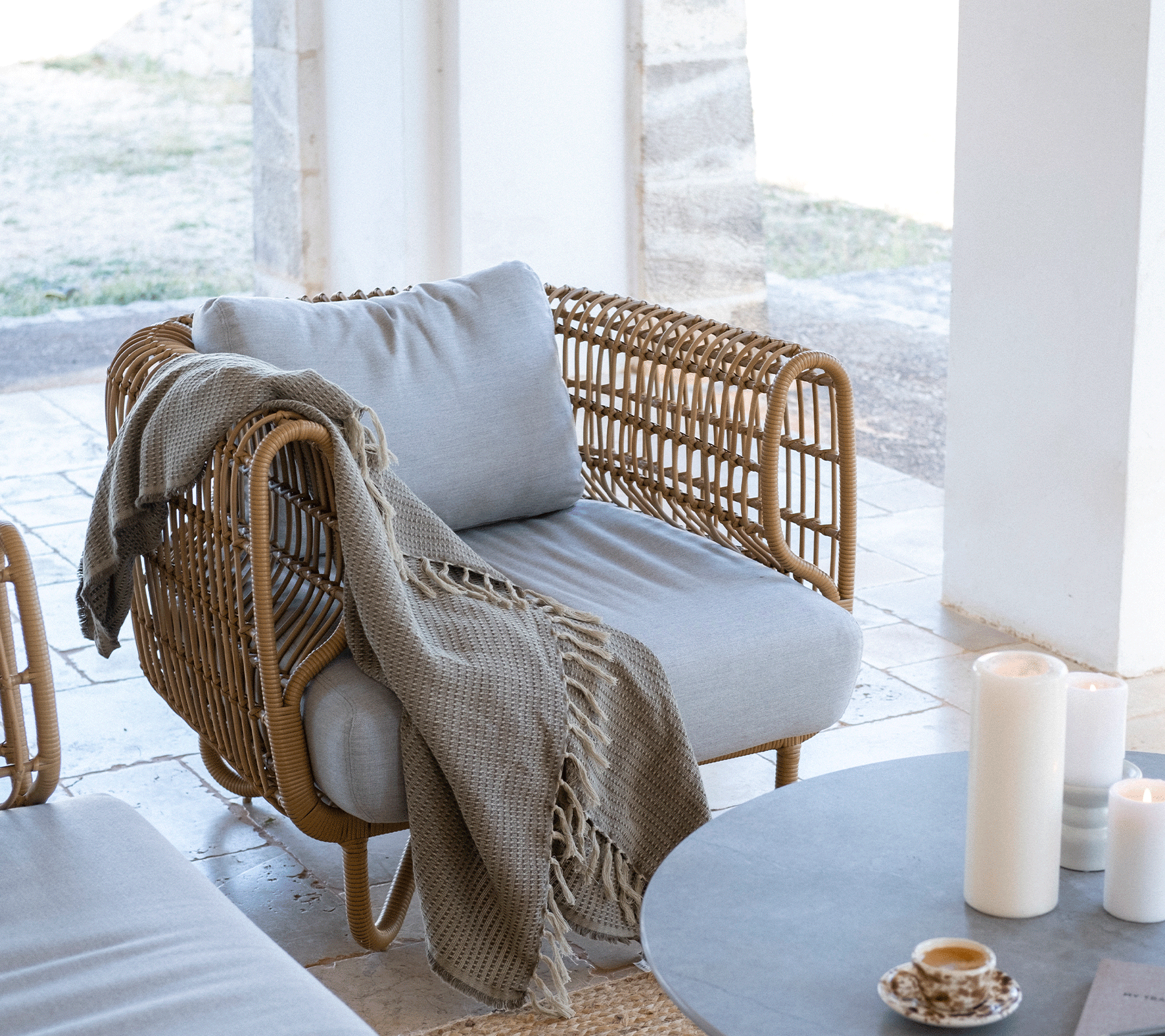 Chaise moderne et confortable avec coussin gris clair, un jeté tricoté drapé sur le côté, entourée de bougies et d'une décoration de table minimaliste.