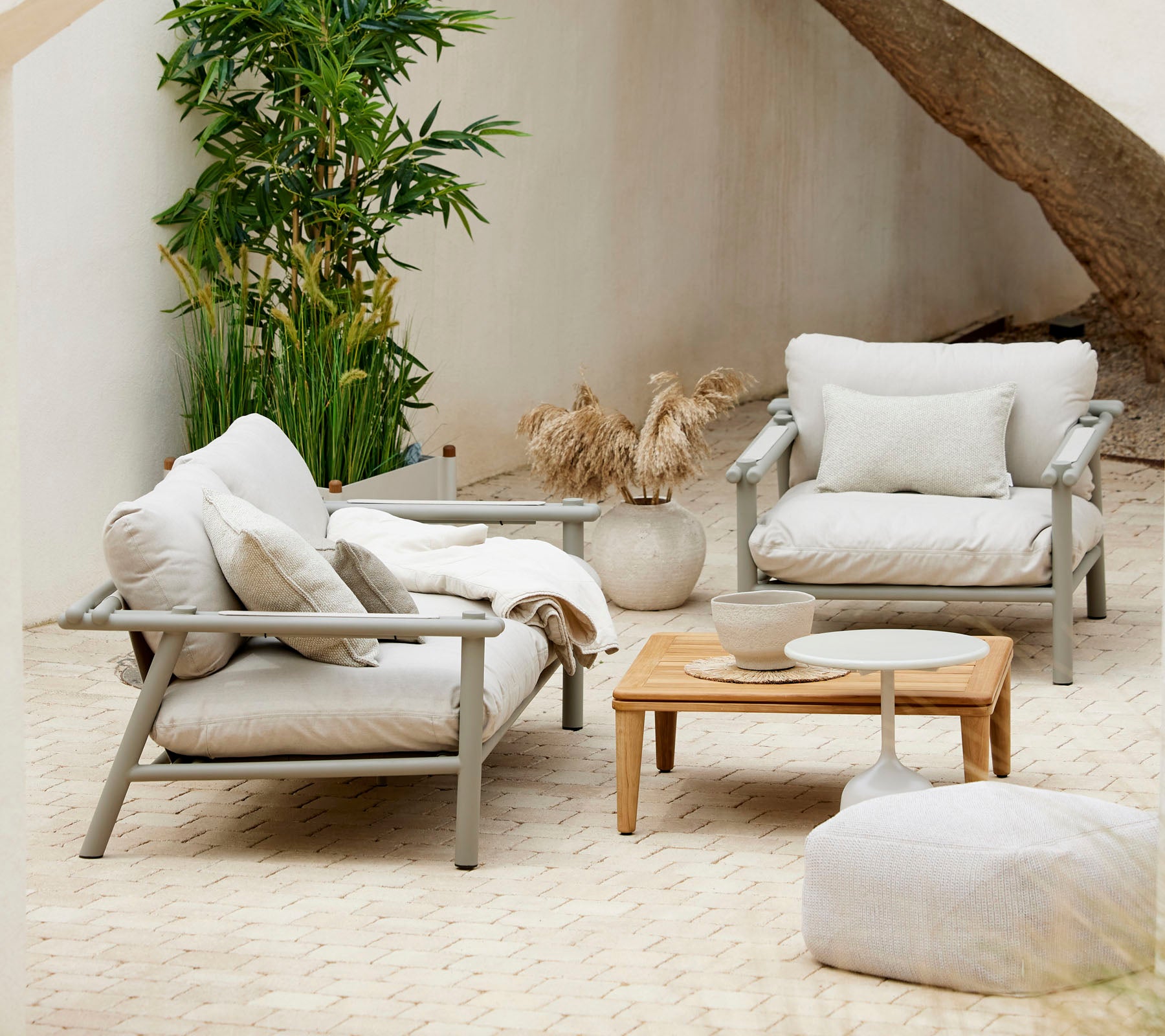 Agencement de sièges douillet avec des coussins moelleux, une table basse en bois et des éléments décoratifs, entouré de verdure.