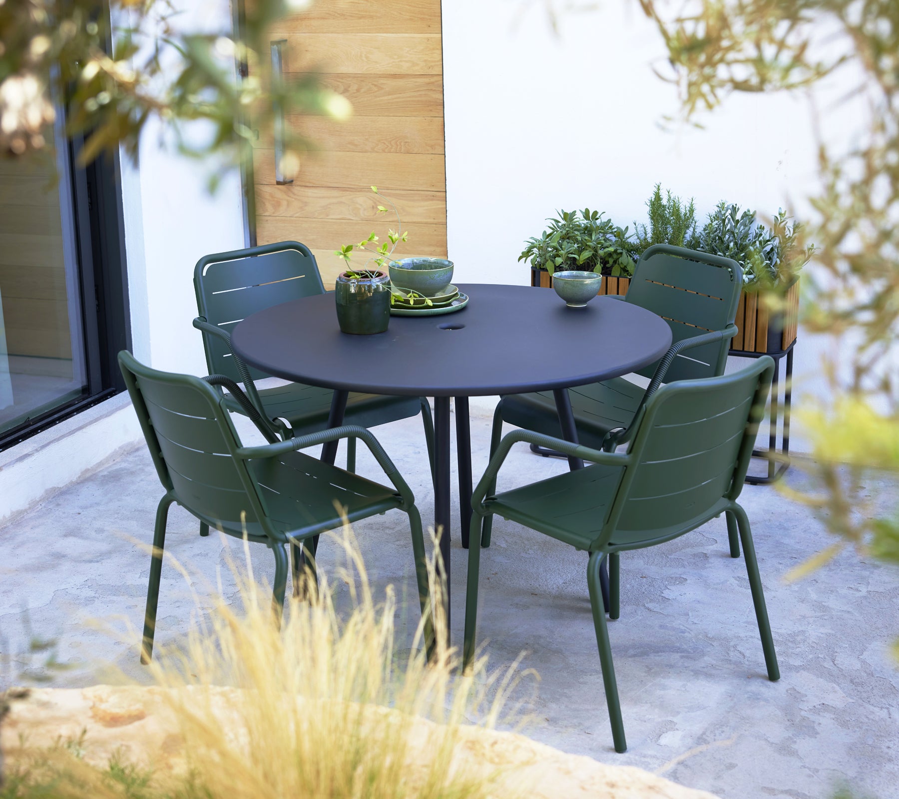Des fauteuils verts de Copenhague disposés autour d'une table ronde noire, complétés par des plats décoratifs et des plantes sur la surface.