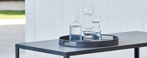Un plateau de service rond contenant divers verre, y compris une grande carafe et plusieurs verres, placé sur une table élégante.