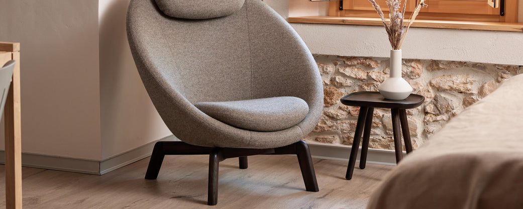 Un fauteuil confortable et moderne complété par une table d'appoint élégante, accentué par un vase et des éléments décoratifs contre un mur texturé.