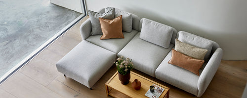 Un canapé gris clair au style élégant avec des coussins confortables, complété par une table basse en bois et une petite plante en pot.