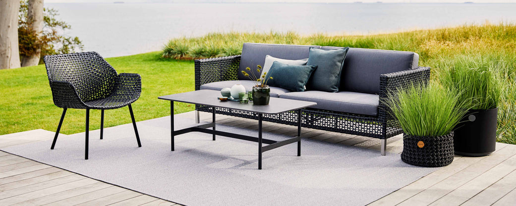 Agencement de sièges élégant comprenant un canapé moderne, un fauteuil et une table basse, complété par des coussins décoratifs et de la verdure.