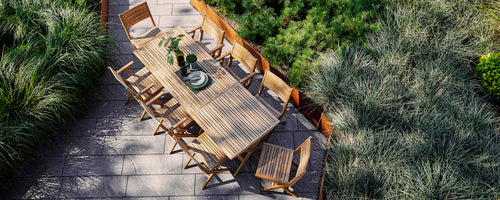 Wooden dining table with chairs surrounded by greenery, featuring a centerpiece with decorative items. Perfect for gatherings.