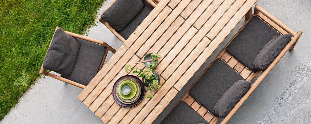 Elegant wooden dining table surrounded by cushioned chairs, featuring a decorative bowl and greenery centerpiece. Perfect for gatherings.
