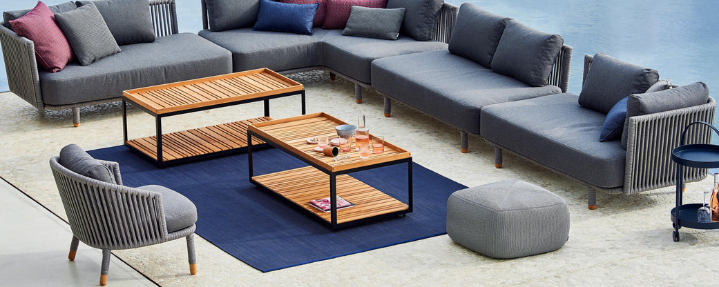 Modern outdoor seating arrangement featuring gray sofas, wooden coffee tables, decorative cushions, and a stylish rug.