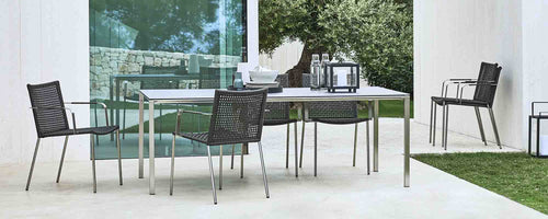 Modern dining setup featuring a sleek table with a pure finish and stylish straw chairs, surrounded by greenery. Perfect for gatherings.
