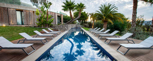 Une rangée de chaises longues à côté d'une piscine réfléchissante, entourée d'une végétation luxuriante et de palmiers, créant un espace de détente serein.