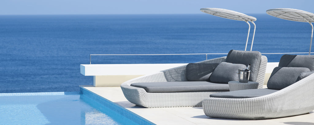 Lounge chairs beside a serene pool overlook a vast blue ocean, creating a tranquil and inviting atmosphere.