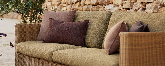 Un coin salon confortable avec des coussins texturés verts et des coussins décoratifs dans des nuances de violet et de brun sur fond de pierre.