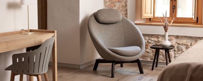 Espace de vie confortable avec une chaise moderne au design arrondi, une petite table d'appoint et un bureau minimaliste. La lumière naturelle entre par une fenêtre.