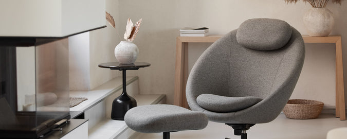 Fauteuil grise confortable avec un repose-pieds assorti à côté d'une table moderne et d'éléments décoratifs, créant un espace élégant et accueillant.