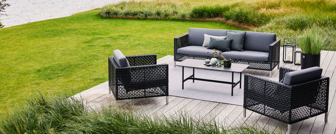 Agencement extérieur élégant avec un canapé gris et deux fauteuils autour d'une table basse, entouré d'une verdure luxuriante.