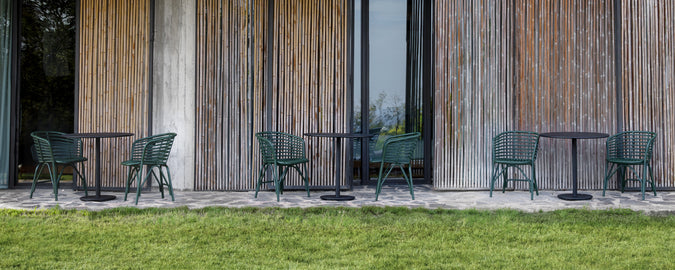 Des chaises vertes et des tables noires disposées à l'extérieur contre un mur en bois.