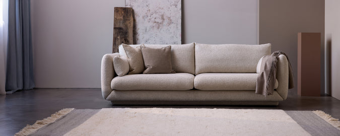 Canapé beige moderne avec des coussins et un jeté gris dans un cadre de salon minimaliste.