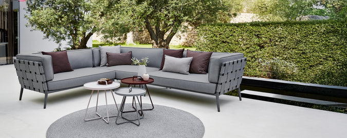 Canapé d'angle moderne gris avec des coussins violets et une table basse ronde dans un espace lounge.