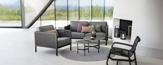 Espace lounge moderne avec un canapé gris, un fauteuil noir et une table basse ronde.